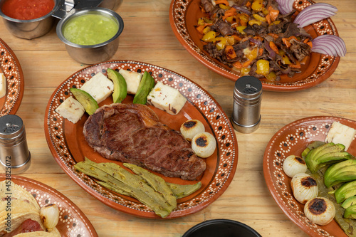 Mexican food, cut of meat served on a plate with nopal, avocado and onion on a wooden table photo