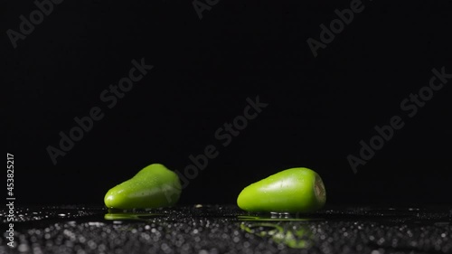 Green hot jalapeno peppers hitting a wet surface bounce upward and form a spray against a black studio background. Wallpaper spicy ripe vegetable for cooking or restaurant. Close up. Slow motion. photo