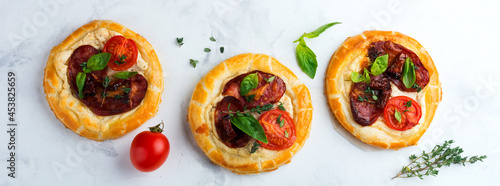Mini tarts with dried meat, tomatoes, ricotta, thyme, basil and olives on a light background. Selective focus.Top view