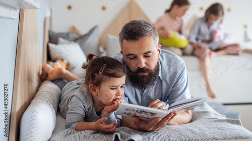 Cuadro en lienzo Father with three daughters indoors at home, reading a book.