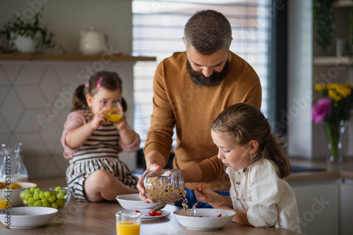 Father with three daughters indoors at home, eating breakfast in kitchen.