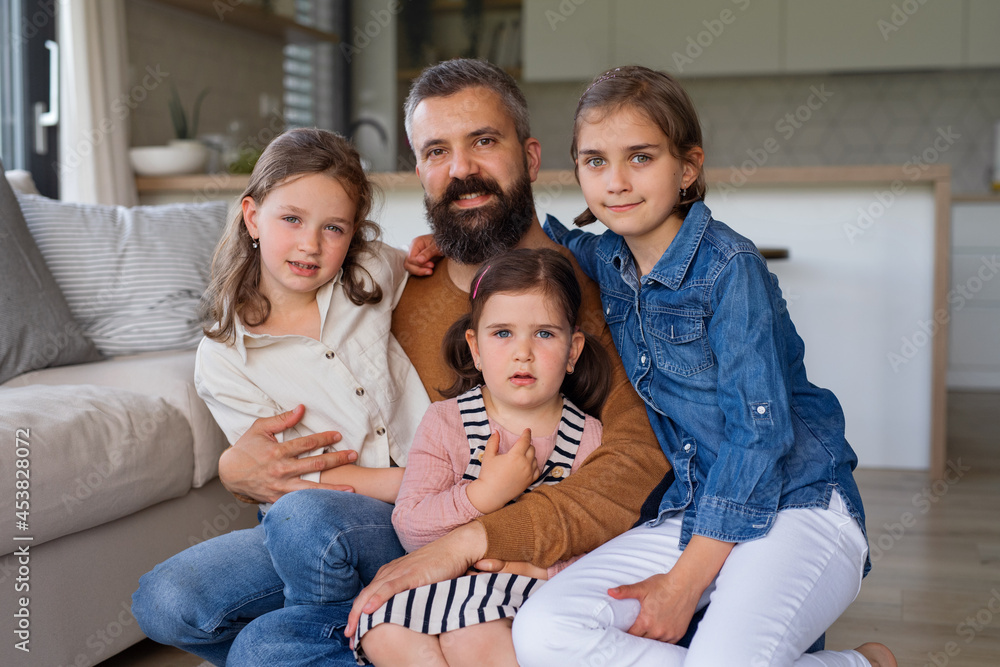 Father with three daughters indoors at home, looking at camera.