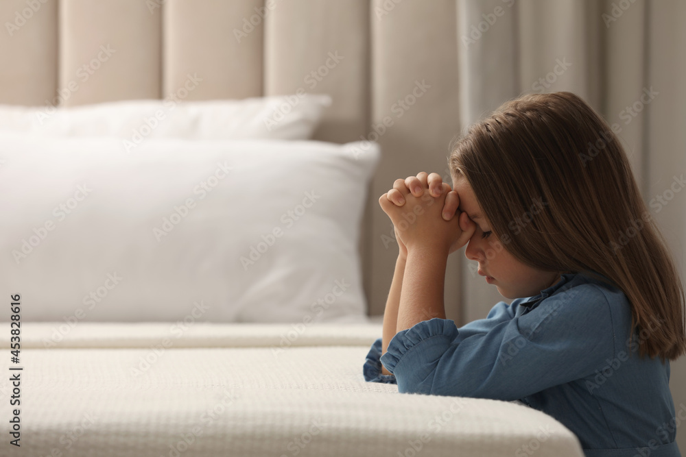 Cute little girl with hands clasped together saying bedtime prayer in bedroom. Space for text Cute little girl with hands clasped together saying bedtime prayer in bedroom. Space for text