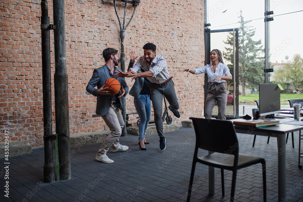 Fototapeta premium Group of cheerful young businesspeople playing basketball in office, taking a break concept.