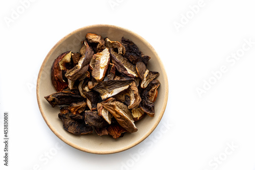 Closeup of dried mushrooms. Sliced boletus edulis in a light brown ceramic bowl isolated on white background. Selective focus on the food, blurred background.