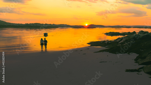 The silhouette of two people on the beach as the sun sets.
