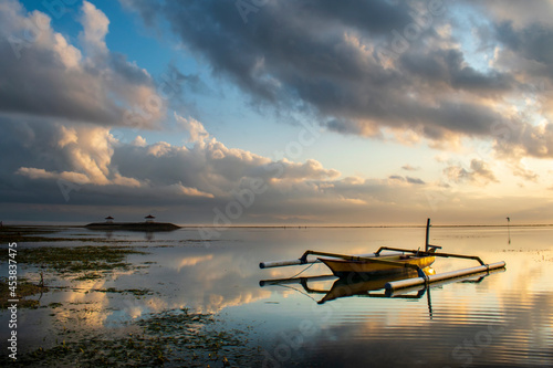 Fishing boat at sunrise Bali coral beach, on the seascape background