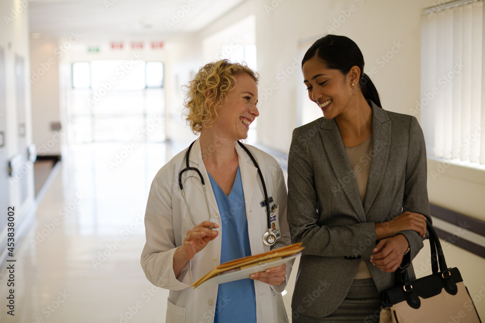 Doctor and businesswoman walking in hospital corridor Doctor and businesswoman walking in hospital corridor
