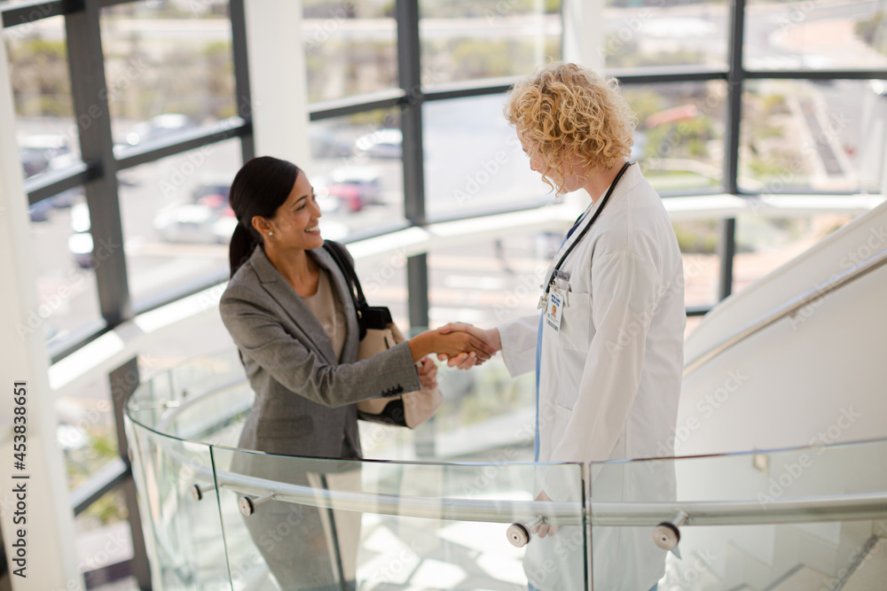 Obraz premium Doctor and businesswoman handshaking on stairs in hospital