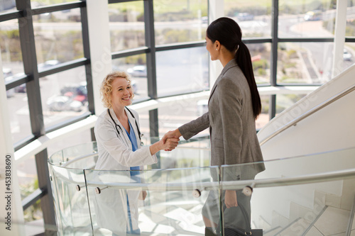 Doctor and businesswoman handshaking on stairs in hospital