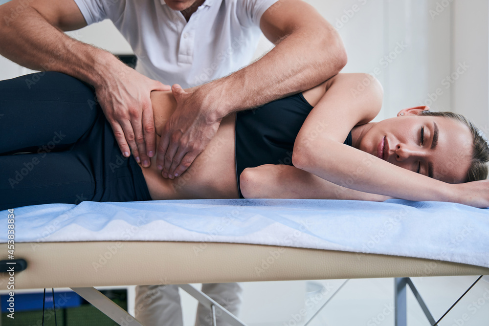 Fototapeta premium Unrecognized male physiotherapist working with woman stomach in medical office