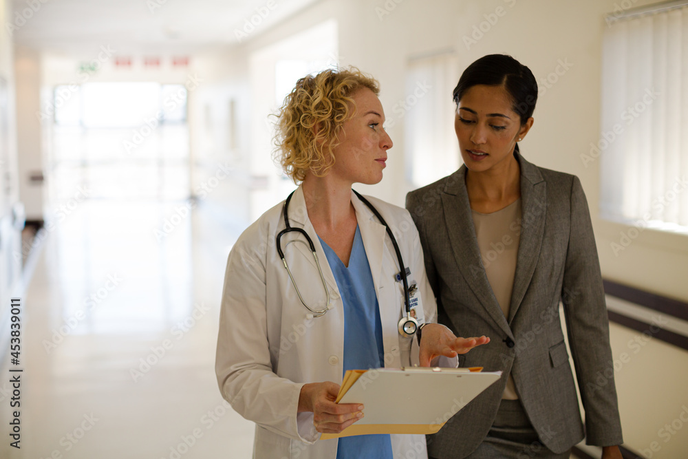 Doctor and businesswoman walking in hospital corridor Doctor and businesswoman walking in hospital corridor