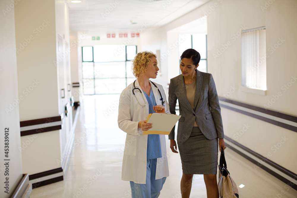 Doctor and businesswoman walking in hospital corridor Doctor and businesswoman walking in hospital corridor