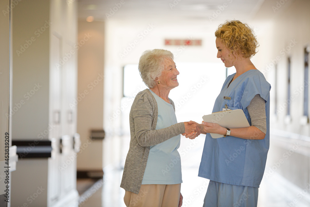 Nurse and senior patient shaking hands in hospital corridor Nurse and senior patient shaking hands in hospital corridor