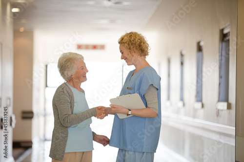 Nurse and senior patient shaking hands in hospital corridor