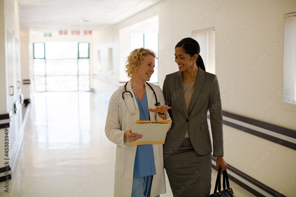 Doctor and businesswoman walking in hospital corridor Doctor and businesswoman walking in hospital corridor