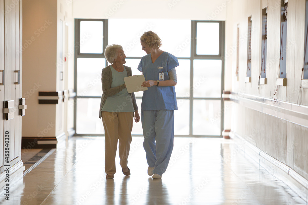 Nurse and aging patient reading chart in hospital corridor