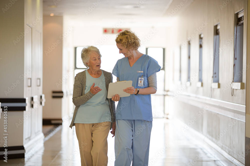 Fototapeta premium Nurse and aging patient reading chart in hospital corridor