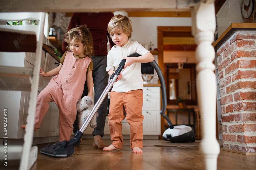Unrecognizable father with two small children hoovering indoors at home, daily chores concept.