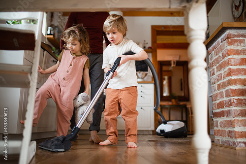 Unrecognizable father with two small children hoovering indoors at home, daily chores concept. photo