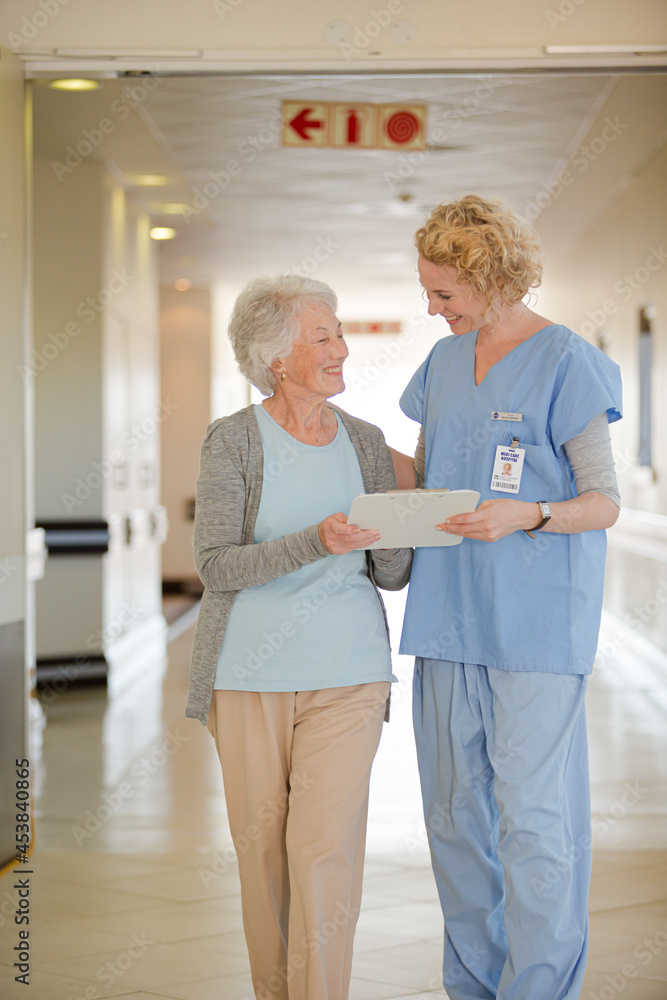Fototapeta premium Nurse and aging patient reading chart in hospital corridor