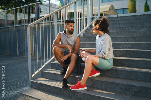 Fototapeta Naklejka Na Ścianę i Meble -  Man and woman friends sitting on stairs outdoors in city, talking after exercise.