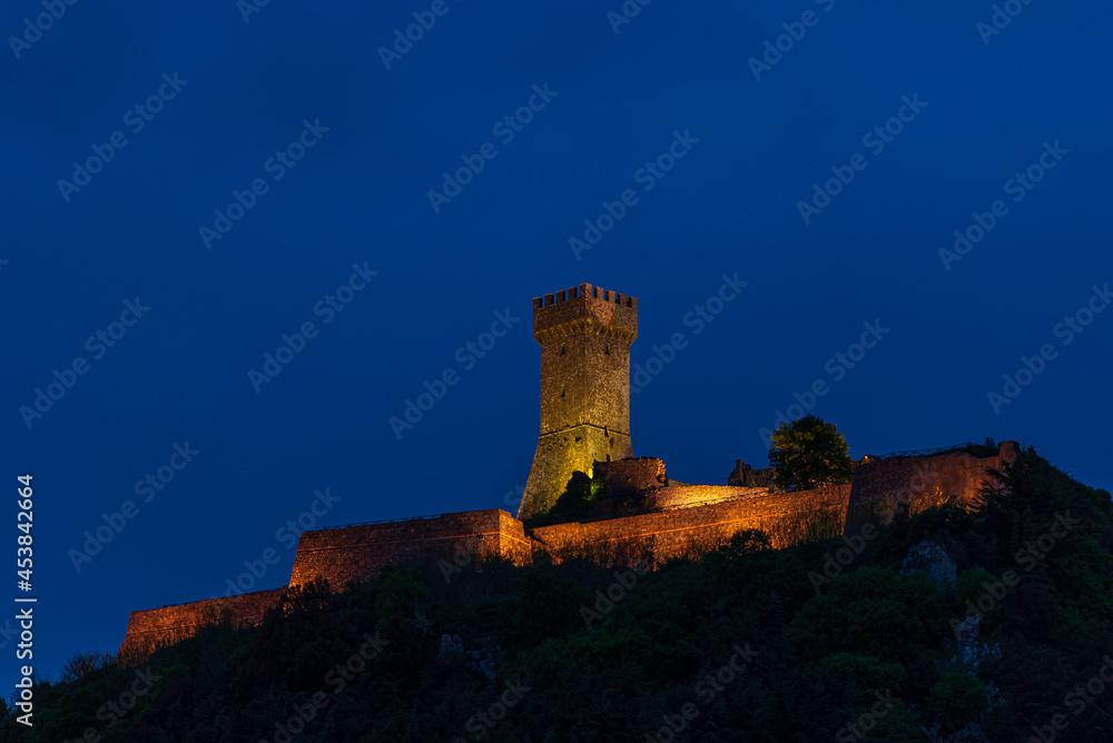 Obraz premium Radicofani, a medieval village and fortress in Tuscany, Italy. Unique view at dusk, the stone tower perched on rock cliff illuminated at dusk against blue sky.