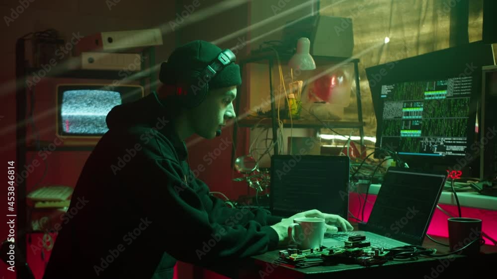 Hacker typing on keyboard at night, breaking password, wearing headphones with microphone. Young man speaking, developing program in dark room. Programmer infecting system with cyber virus Hacker typing on keyboard at night, breaking password, wearing headphones with microphone. Young man speaking, developing program in dark room. Programmer infecting system with cyber virus