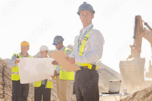 Workers reading blueprints by digger in quarry