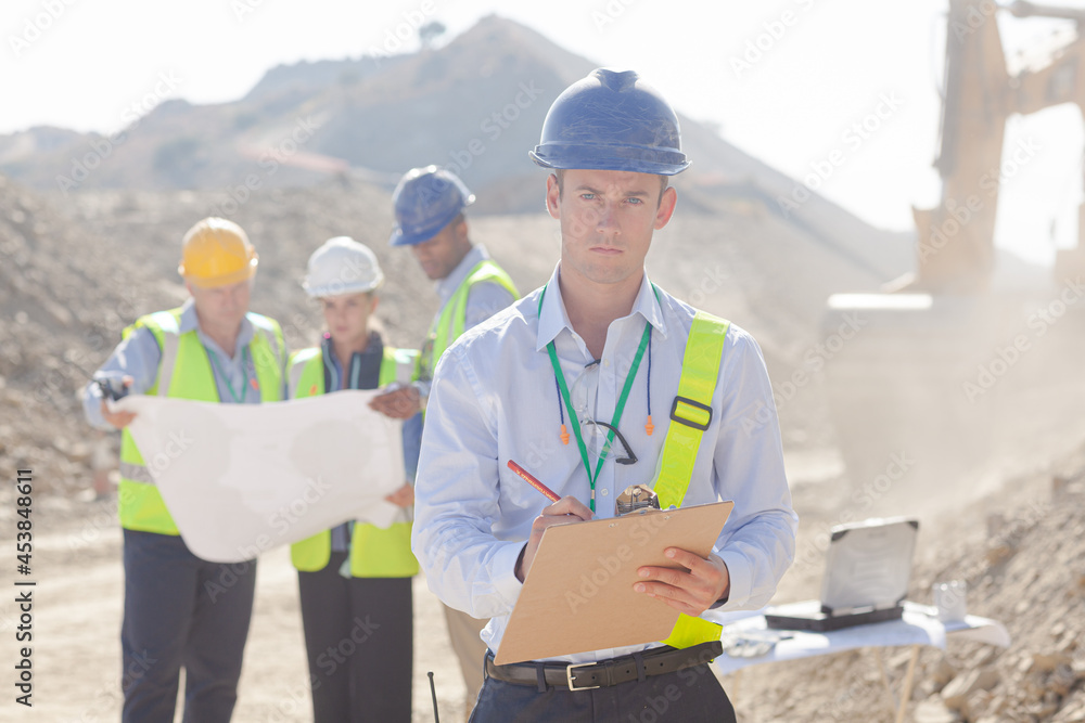 Workers and businessman reading blueprints in quarry Workers and businessman reading blueprints in quarry