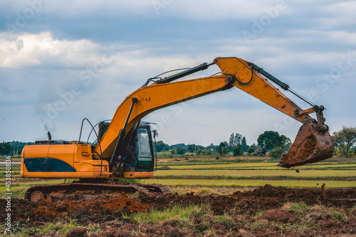 Backhoe or excavator working on land of countryside, excavator dig soil in rice field site industry, blue sky and green field agriculture background