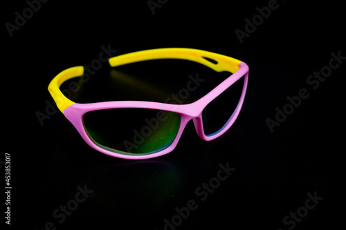 Children's glasses for cycling and sports. Made of pink plastic with yellow temples and UV-resistant lenses. Photographed on a black background.