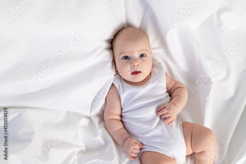 portrait of a child on a white bed in the morning. Textiles and bed linen for children. A newborn baby has woken up or is going to bed