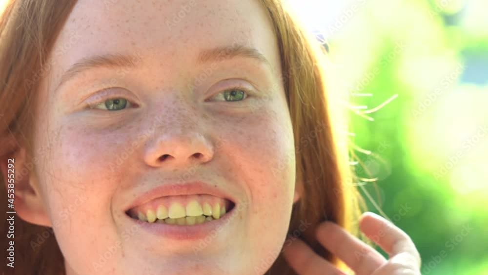 Face of a young woman with red hair and freckles on a background of green foliage. Natural beauty with freckles Face of a young woman with red hair and freckles on a background of green foliage. Natural beauty with freckles
