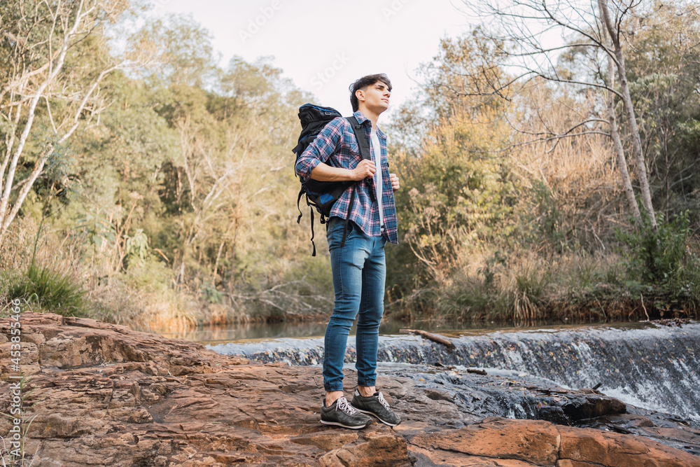 Traveling man standing near small waterfall in woods Traveling man standing near small waterfall in woods