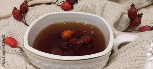 white cup of tea with rose hips on a soft woolen blanket.