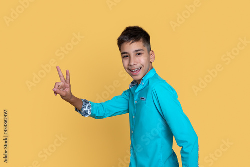 Young smiling teenage boy  gestures a sign  victory or pease against a yellow background. photo