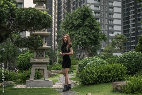 Beautiful slim young asian woman in black mini dress walking in the park. Long hair. Nice posture. Side view. Picture from the side.