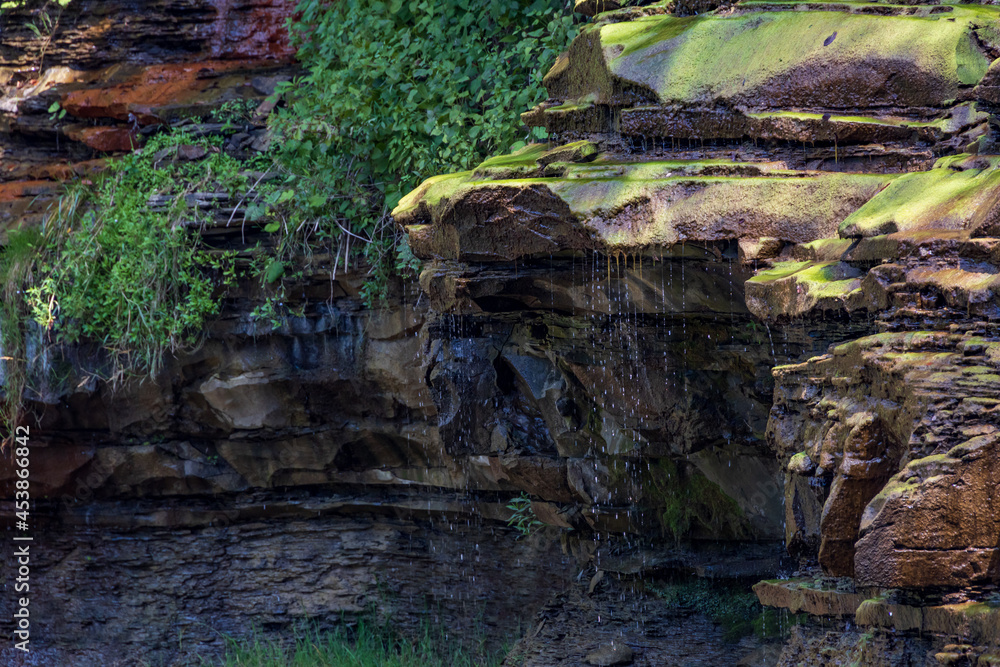 Fototapeta premium Water dripping over rock ledge covered in moss