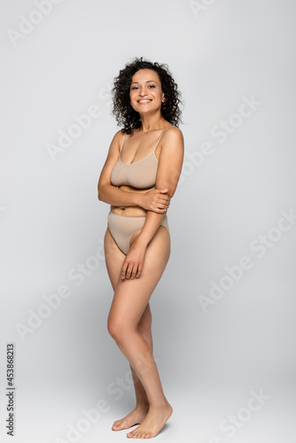 Smiling african american woman in bra and panties standing isolated on grey