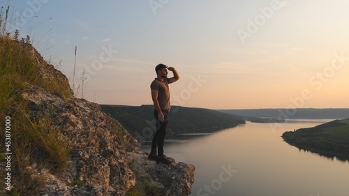 The young man stands on rocky mountain on beautiful river background