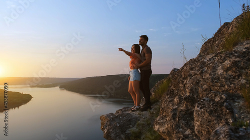 The young couple standing on rocky mountain above the beautiful river