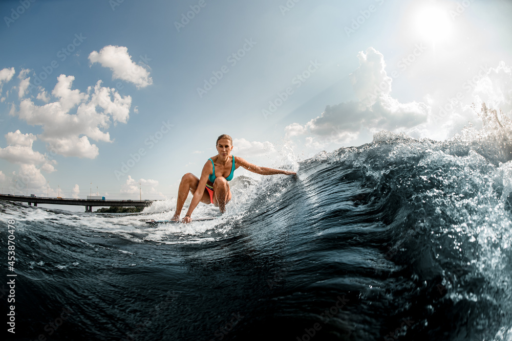 active young woman rides down the wave on a wakeboard