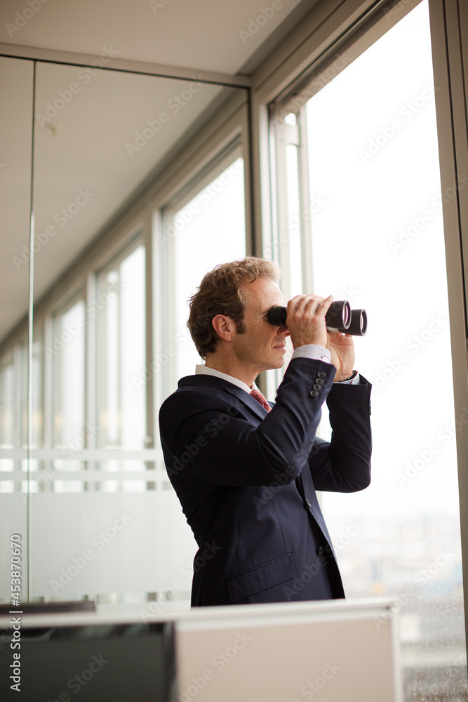 Businessman using binoculars at office window Businessman using binoculars at office window