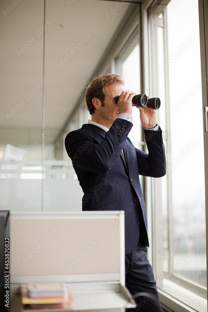 Businessman using binoculars at office window Businessman using binoculars at office window