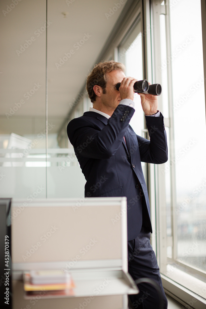 Businessman using binoculars at office window Businessman using binoculars at office window