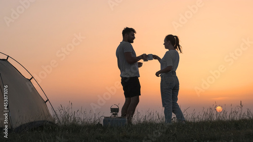 The romantic couple sitting near the campsite tent and preparing tea