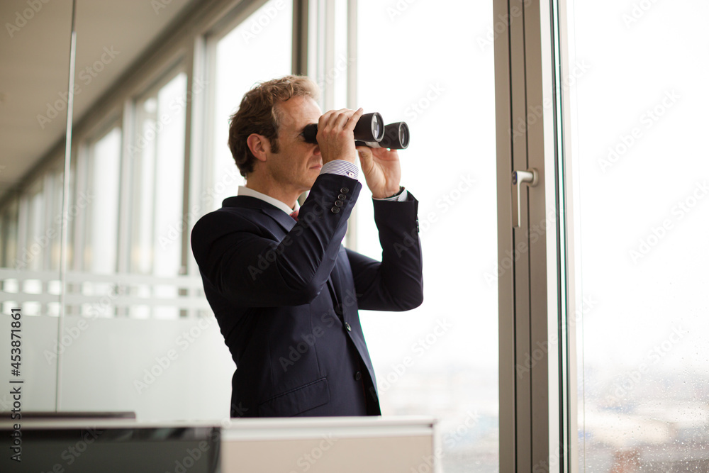 Businessman using binoculars at office window Businessman using binoculars at office window