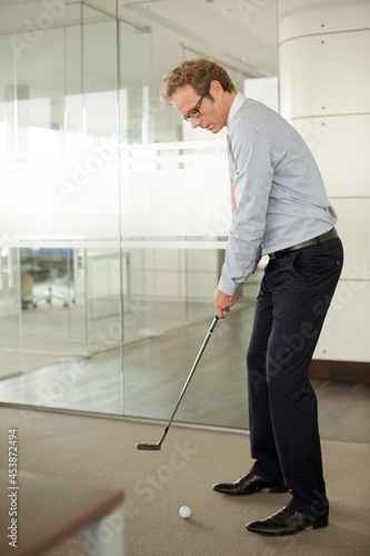 Businessman putting golf ball in office
