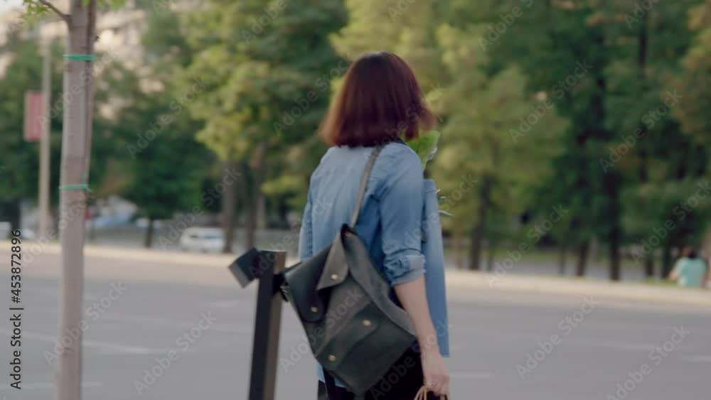 Middle aged woman with paper shopping bags with buying plant, walking through outdoor parking lot Middle aged woman with paper shopping bags with buying plant, walking through outdoor parking lot